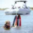 Woman holding two water skis with a boat in the background on a lake
