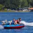 Three people on a blue and red Ultra Screamer tube in the water with a blurred background of trees and houses.