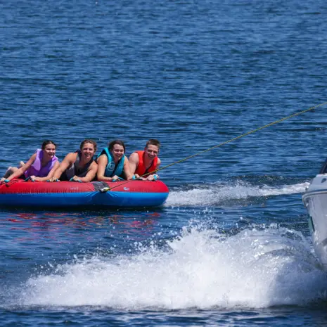 Obrien X Scream Boat Tube Lifestyle 04 People on a red and blue X-Scream inflatable tube being pulled by a boat on water.