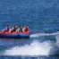 People on a red and blue X-Scream inflatable tube being pulled by a boat on water.