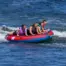 Four people on a red and blue X-Scream towable tube in the water.