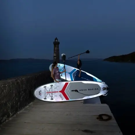 Aqua Marina illuminated paddle board - people holding illuminated boards beside the water at dusk Aqua Marina illuminated paddle board - people holding illuminated boards beside the water at dusk