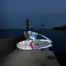 Aqua Marina illuminated paddle board - people holding illuminated boards beside the water at dusk
